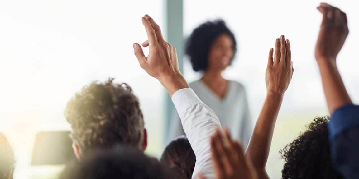 Professora ministrando aula presencial, enquanto a turma levanta a mão para fazer perguntas, após ela empreender e descobrir quanto custa abrir uma escola de cursos?