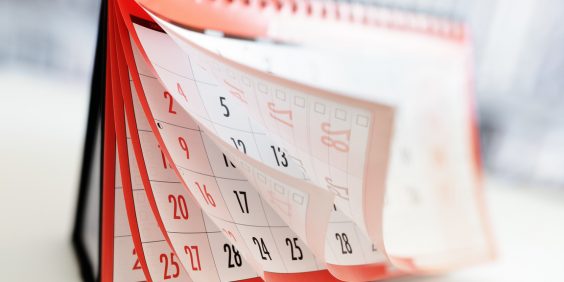 A imagem mostra um calendário de mesa de bordas vermelhas sendo folheado.